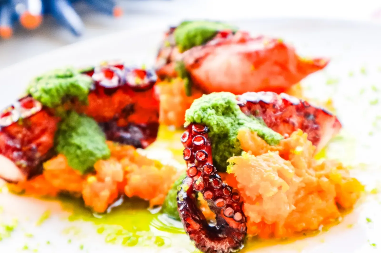 Polpo arrostito con salsa verde e purea arancione, ripreso da vicino con lo sfondo sfocato