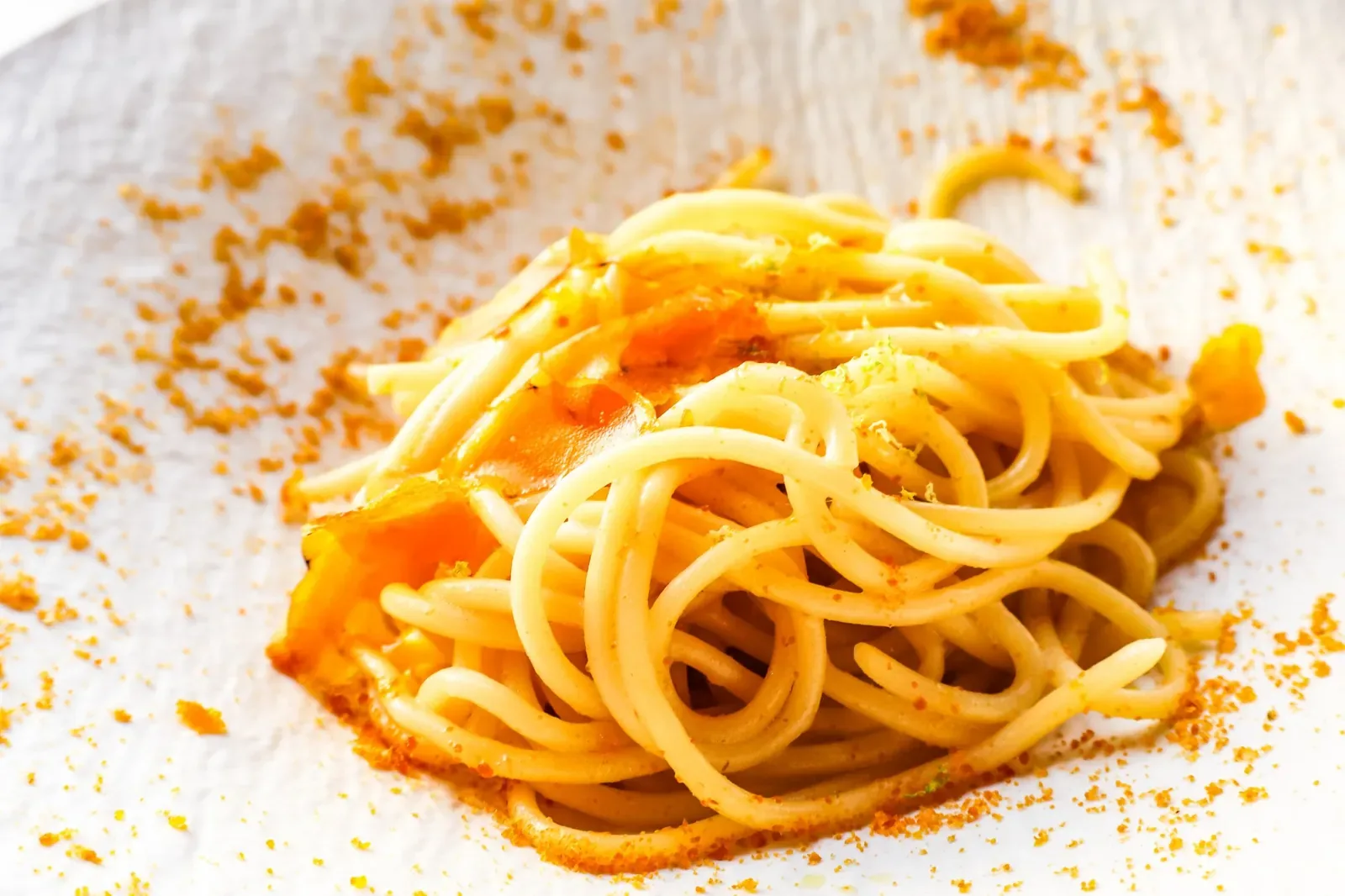Spaghetti alla bottarga con scorza di limone in un piatto bianco lavorato, visti da vicino